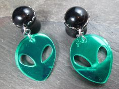 "This pair of dangle plugs features jet black round gems, set in closed silver plated scalloped frames. Dangling from each is a green acrylic mirror-finish alien head charm, which is grey on the back side. These are available in the following sizes and styles: 12g (2mm) - Steel Screw Back 10g (2.4mm) - Steel Screw Back 8g (3mm) - Steel Screw Back 8g (3mm) - Acrylic Screw Back 6g (4mm) - Steel Screw Back 6g (4mm) - Acrylic Screw Back 4g (5mm) - Black Acrylic Screw Back 4g (5mm) - Steel No Flare w Black Round Novelty Jewelry, Novelty Black Round Jewelry, Unique Green Plug Earrings, Dangle Plugs, Alien Head, Green Mirror, Plug Earrings, Green Mirrors, Jewelry Tattoo