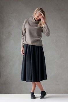 a woman in a gray sweater and black pleated skirt is posing for the camera