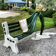 a green and white bench sitting on top of a gravel covered ground next to a lush green park