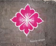 a pink and white flower painted on the side of a cement wall with words rupa's rangoli written below it