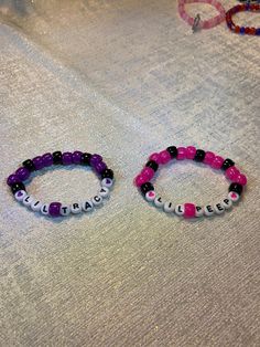 two bracelets sitting on top of a bed covered in white and purple beads next to each other