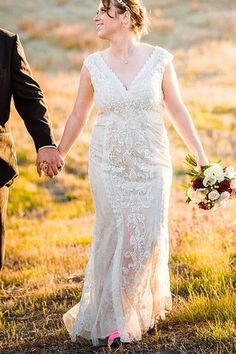 a bride and groom hold hands as they walk through an open field in the sun