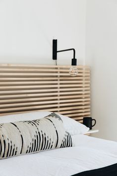 a white bed with black and white pillows on top of it next to a wooden headboard