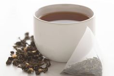 a cup of tea next to a pile of loose leafed ooloy on a white surface