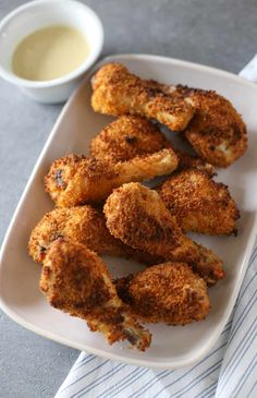 some fried food on a white plate next to a bowl of sauce and a napkin