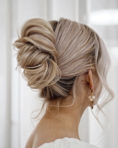 a woman with blonde hair in a low bun, wearing gold earrings and a white dress