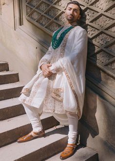 a man standing on some steps wearing a white outfit with green accents and beaded necklaces