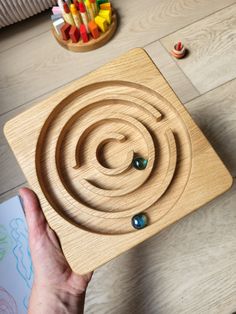 a person holding up a wooden puzzle with colored pencils in the background and a box of crayons next to it