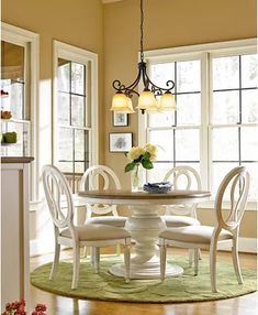 a dining room table with four chairs and a vase on top of it in front of two windows