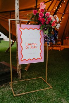 a sign that is sitting in the grass with flowers on it and lights behind it