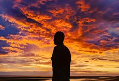 the silhouette of a person standing in front of a colorful sky with clouds at sunset