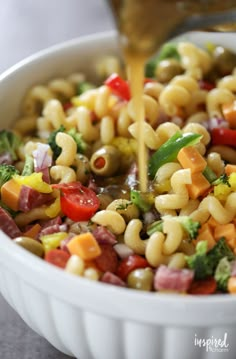 a white bowl filled with pasta salad being drizzled on top of it