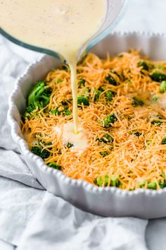 broccoli and cheese casserole being poured into a white dish with grated cheese