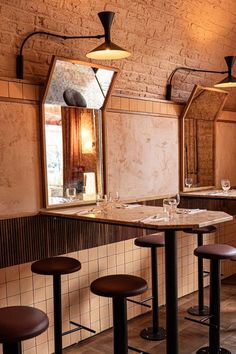 an empty restaurant with stools and tables in front of the bar area, along with two mirrors on the wall