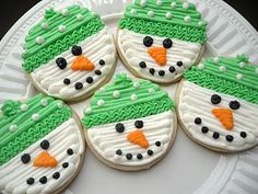 frosted cookies decorated like snowmen on a white plate with green and orange icing