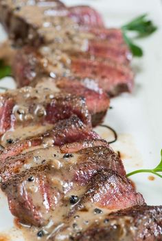 some steaks with sauce on them sitting on a white plate and garnished with green leaves