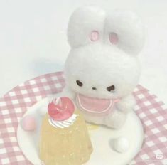 a small white stuffed animal sitting on top of a plate next to a piece of cake