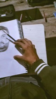 a person holding a pen and drawing on a piece of paper with the image of a man's face