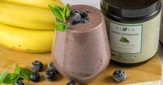 a smoothie with blueberries and mint sits next to bananas on a cutting board