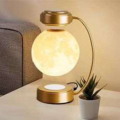 the moon lamp is sitting on top of a table next to a potted plant