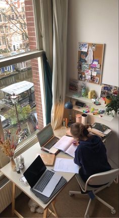 a person sitting at a desk in front of a window working on a laptop computer