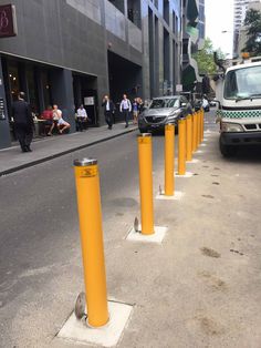 there are yellow poles on the side of the street with cars parked in front of them