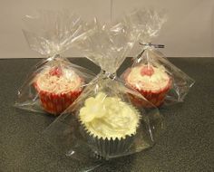 three cupcakes wrapped in plastic sitting on a counter