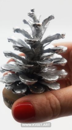 a hand holding a silver pine cone on it's fingers