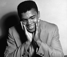 a black and white photo of a man smiling with his hands to his face,