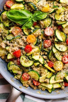 a bowl filled with zucchini and tomatoes on top of a striped table cloth