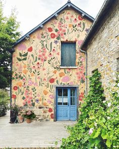 an old building with flowers painted on it's side and a blue door in front