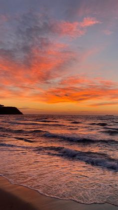 the sun is setting over the ocean with waves coming in to shore and an island in the distance