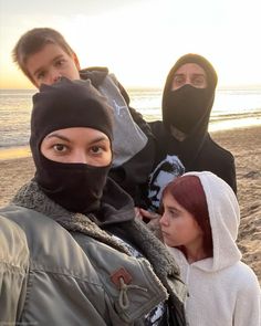 three people standing on the beach wearing ski masks