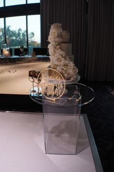 a wedding cake with white flowers on display in front of a large window at night