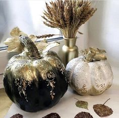 three decorative pumpkins sitting next to each other on a table with dried leaves in front of them