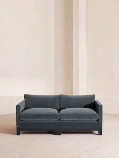 a gray couch sitting on top of a hard wood floor next to a white wall