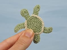 a hand holding a tiny crocheted turtle