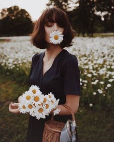 a woman standing in a field with daisies on her face and holding a basket