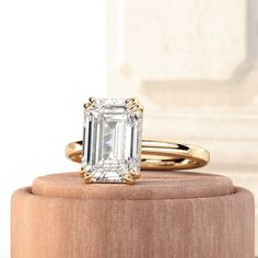 an emerald cut diamond ring sitting on top of a wooden stand