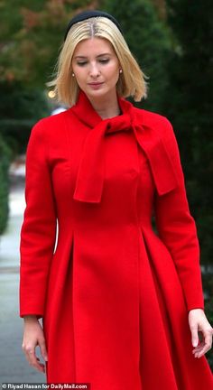 a woman in a red coat is walking down the street with her hand on her hip