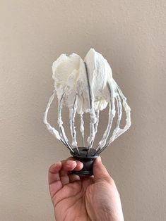 a hand holding a wire whisk in it's palm with white icing