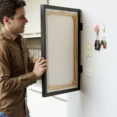 a man is holding up an empty board in front of the refrigerator door with magnets on it