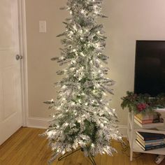 a white christmas tree with lights and snow on it in front of a flat screen tv