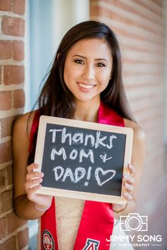 a woman in a graduation gown holding a chalkboard that says thanks mom and dad