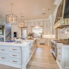 a large kitchen with white cabinets and an island in the middle of it is lighted by pendant lights