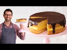 a man standing next to a cake with chocolate icing on it