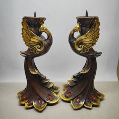 two decorative candlesticks made out of wood and gold leafy designs, each with a candle holder in the shape of a peacock