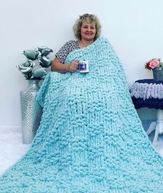 a woman is wrapped up in a blue blanket and holding a coffee mug while sitting on a chair