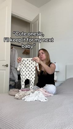 a woman sitting on top of a bed holding up a baby's shirt with the words, cute onesie, i'll keep it for my next baby