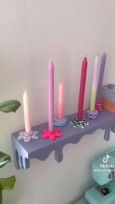 candles are lined up on a shelf in front of a white wall and green plant